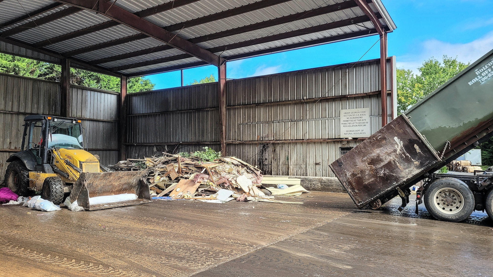 Dump truck has dumped Trash in shed and bulldozer will move it for disposal.